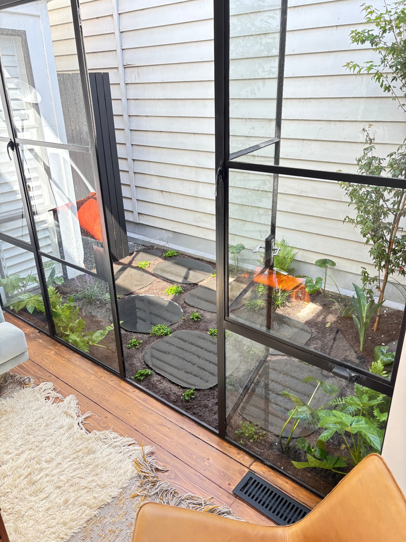 A compact light-well courtyard reimagined as a leafy retreat — organic-form bluestone steppers set into soft mulch, layered ferns and shade-loving understorey, an integrated drip irrigation system, and a charcoal rendered privacy screen wrapping the boundary.